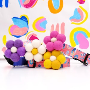 Puede incluir: Cuatro collares coloridos para perros con detalles de flores de fieltro. Los collares presentan un estampado de leopardo rosa y están adornados con flores de fieltro moradas, blancas, rosas y amarillas. Fondo con arte abstracto colorido.