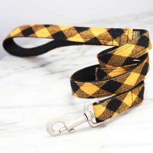 May include: A black and yellow plaid dog leash with a silver clip.