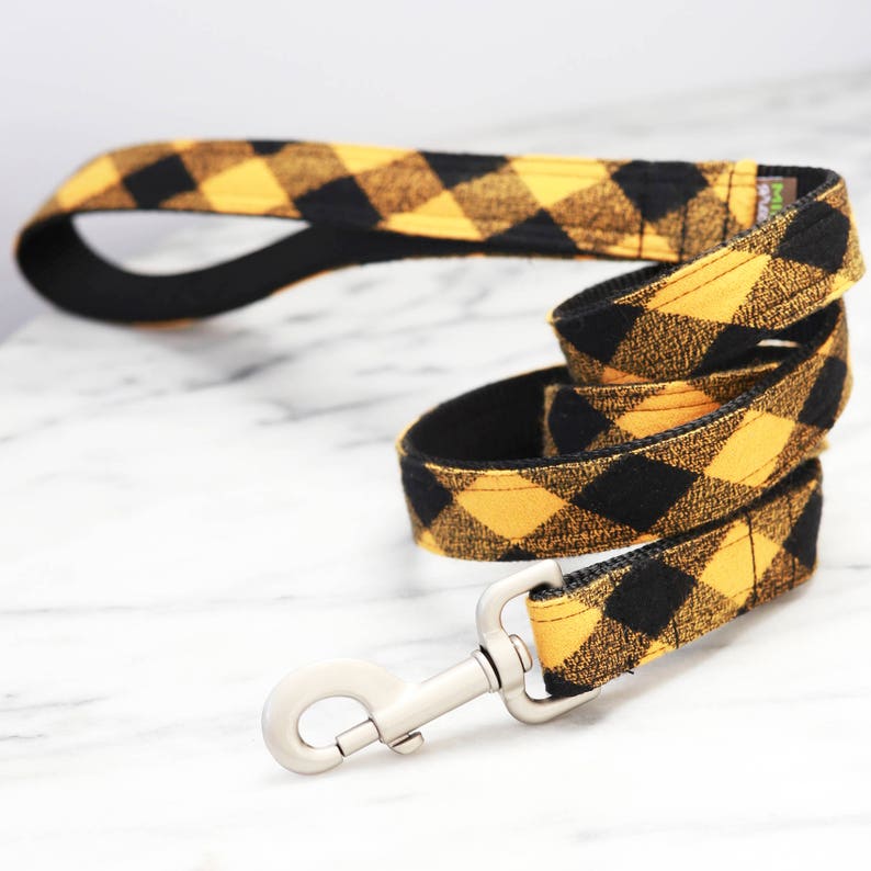 May include: A black and yellow plaid dog leash with a silver clip.