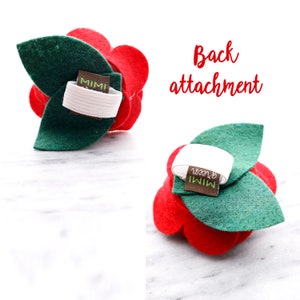 May include: Red felt flower hair clip with green felt leaves. The back of the clip has a white elastic band and a brown label that says "Mimi Green".