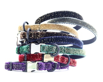 May include: A stack of six colorful velvet cat collars with glitter. The collars are in shades of purple, red, green, blue, brown, and gold. Each collar has a silver buckle.