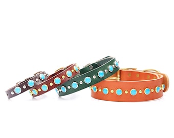 May include: Four leather dog collars in varying shades of brown and green. Each collar is adorned with turquoise-colored stones and metal studs. The collars have brass or silver-colored buckles and hardware.