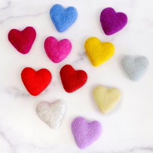 May include: Ten felt hearts in various colors, including red, pink, purple, blue, yellow, and gray, arranged on a white marble surface.