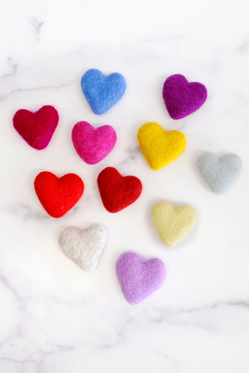 May include: Ten felt hearts in various colors, including red, pink, purple, blue, yellow, and gray, arranged on a white marble surface.
