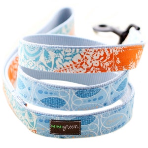May include: A blue and orange dog leash with a white floral pattern. The leash has a blue and white patterned fabric on the underside. The leash has a brown tag with the text "MIMIGreen" on it.