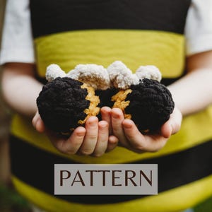 May include: A child's hands holding two crocheted bee toys. The bees are black and yellow with white wings. The child is wearing a yellow and black striped shirt. The text "PATTERN" is printed on a brown rectangle below the image.