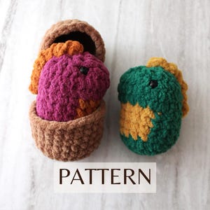 May include: Two crocheted dinosaur toys, one in a brown crocheted basket. The dinosaur in the basket is purple and orange, while the other dinosaur is green and yellow.