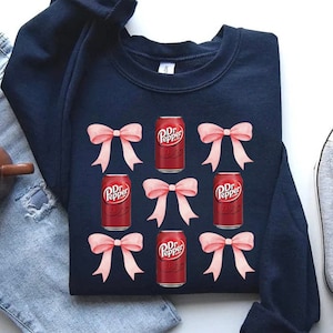 May include: A navy blue sweatshirt with a pattern of six pink bows and six red and white Dr Pepper cans.