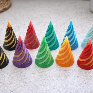 May include: A collection of ten colorful, cone-shaped party hats. Each hat features a spiral design with a different color scheme, including black and gold, purple and gold, and various shades of red, green, blue, and orange.