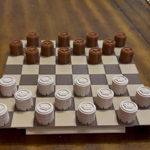 May include: A checkerboard with brown and beige squares. Brown checkers with a circular design are on one side, and beige checkers with a crown design are on the other. The game is set up on a wooden table.