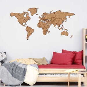 May include: A large, detailed world map made of cork, mounted on a white wall. The map is a light brown color and shows the continents and countries. The map is above a wooden daybed with red pillows and a blanket.