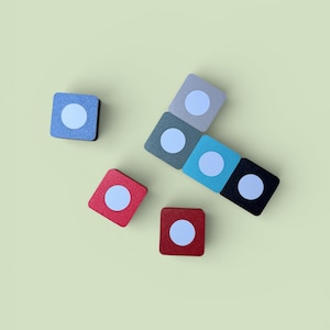以下が含まれることがあります： 白い円が中央にあるカラフルな正方形のブロックがいくつか上から見た写真。ブロックは青、赤、グレー、ティール、黒の色合いで、明るい緑色の背景に配置されています。