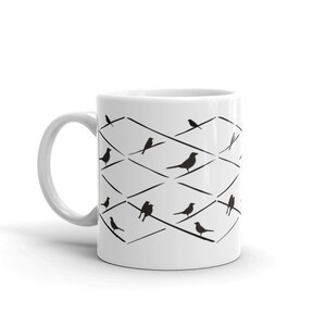May include: White ceramic mug featuring a black and white bird design. The design includes black birds perched on a diamond-patterned wire grid. The mug has a curved handle and a glossy finish.
