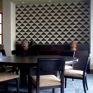 May include: A dining room featuring a dark wood table and chairs. The chairs have tan upholstered seats. The wall is decorated with a repeating pattern of black triangles against a cream background. Decorative vases are on a dark wood shelf.