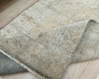 May include: A light beige rug with a fringed edge. The rug is folded in half and the underside is visible.