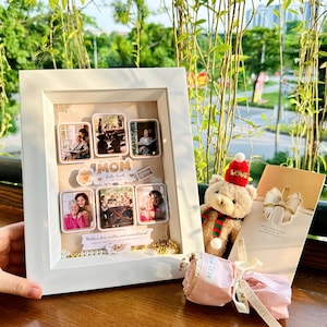 Puede incluir: Un collage de fotos enmarcado en blanco con seis fotos pequeñas, la palabra "MOM" y el texto "Mother's love, endless and unconditional". También hay un oso de peluche con un gorro rojo y una bolsa de regalo.
