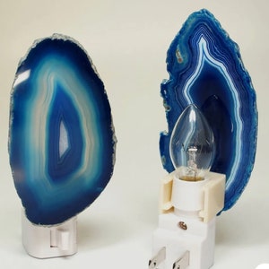 May include: Two blue agate night lights with white plugs. The agate is a natural stone with a blue and white pattern. The night lights are plugged into an electrical outlet.