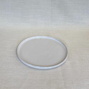 May include: A white ceramic plate with a slightly raised rim. The plate is round and has a smooth, matte finish.