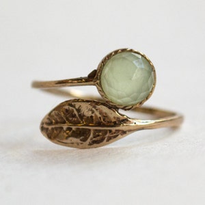 Puede incluir: Un anillo de oro con una piedra preciosa verde y un diseño de hoja.