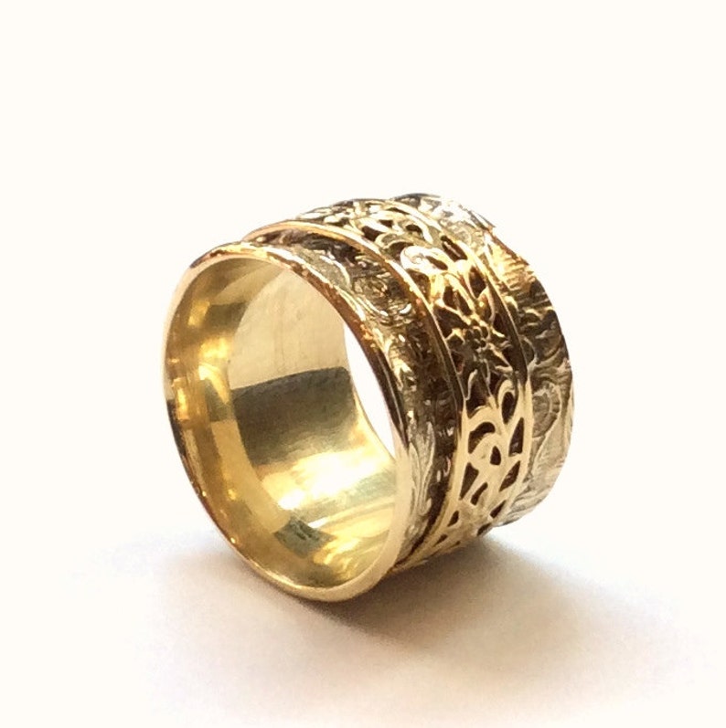 May include: A gold ring with a detailed floral design. The ring is wide and has a smooth, polished finish.
