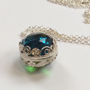 May include: A silver necklace with a teal blue gemstone pendant surrounded by a silver filigree design.