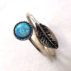 Puede incluir: Un anillo de plata con una piedra de ópalo azul y un diseño de hoja. El anillo está hecho de plata de ley y es una pieza de joyería delicada y elegante.