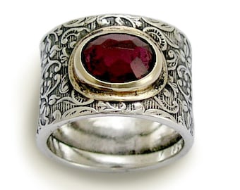Pode incluir: Um anel de prata com um design floral ornamentado e uma pedra preciosa vermelha engastada em uma moldura de ouro.