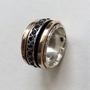 Op de afbeelding: Een draaibare zilveren en gouden ring met een band van blauwe edelstenen.