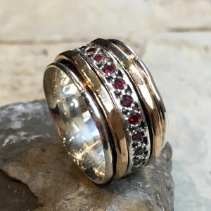 May include: A silver and gold spinning ring with a band of red gemstones.