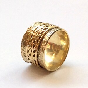 May include: A gold-toned spinning ring with intricate floral designs. The ring is made of metal and has a smooth, polished finish.