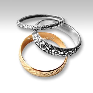 May include: Three silver and gold rings with intricate designs. The top ring has a chevron pattern, the middle ring has a floral design, and the bottom ring has a wavy pattern.