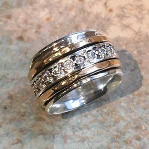 May include: A silver and gold spinning ring with a row of clear stones.