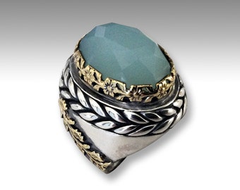 May include: A silver ring with a large, oval-shaped, light green gemstone set in a gold floral design. The ring band is silver with a braided design.