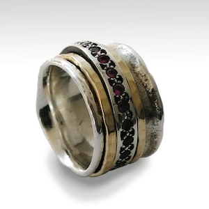 May include: A silver and gold ring with a band of red and black stones. The ring is made of three bands that spin independently.