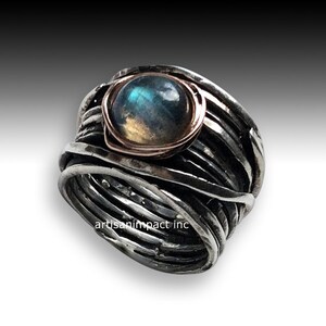 May include: A silver ring featuring a blue and green labradorite gemstone set in a rose gold bezel. The ring is crafted from multiple strands of silver wire that are twisted and woven together.