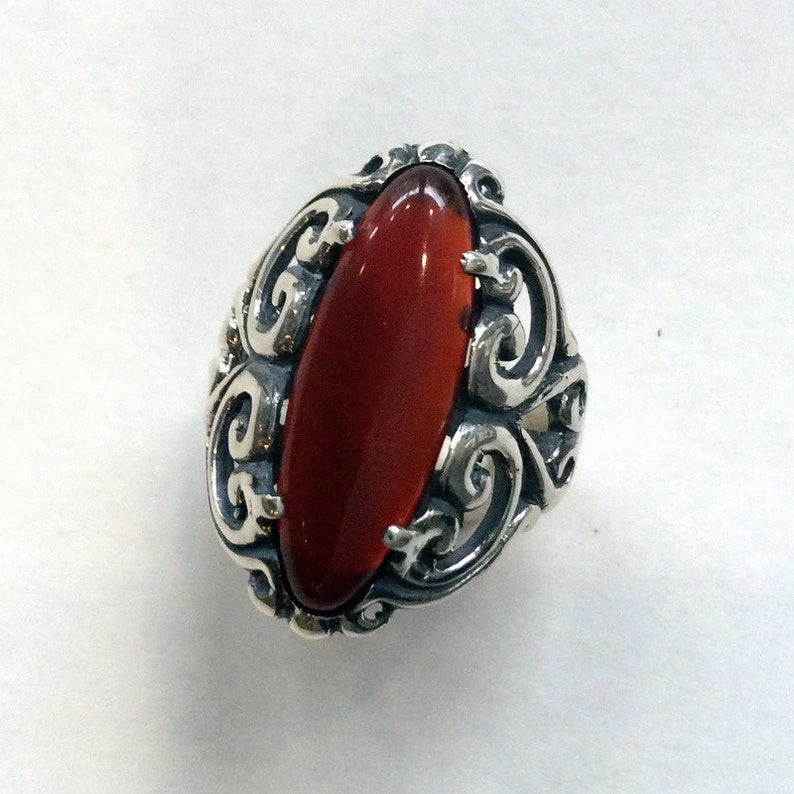 May include: A silver ring with an oval-shaped red gemstone set in a filigree design.
