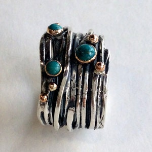 May include: A silver ring with multiple bands, each with a textured finish. The ring is adorned with turquoise stones and gold accents.