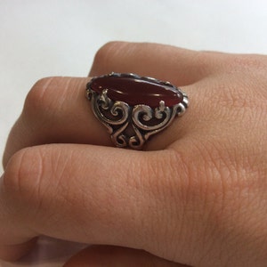 May include: A silver ring with an oval-shaped carnelian gemstone set in a filigree design.