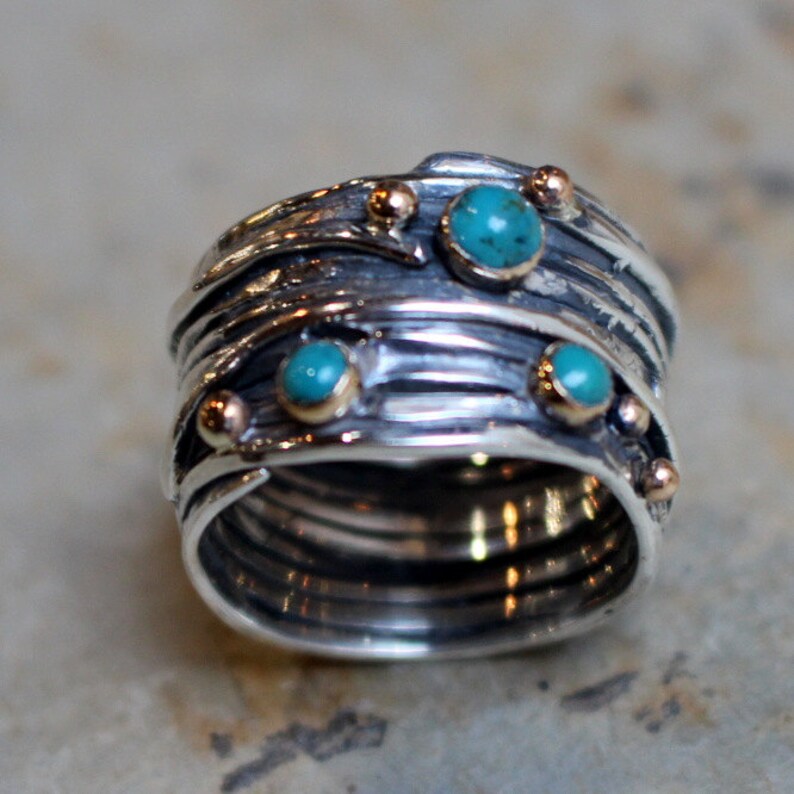 May include: A silver ring with multiple bands, each with a textured surface. The ring is adorned with four turquoise stones and gold accents.