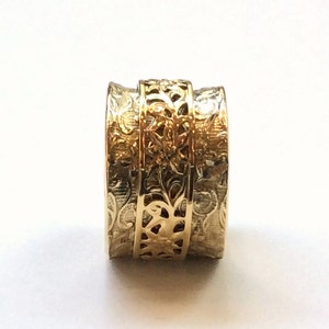 May include: A gold ring with intricate floral designs. The ring is made of two bands, one with a filigree pattern and the other with a textured surface.