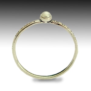 以下が含まれることがあります： 中央に小さな白い真珠がセットされた銀のリング。リングのバンドはテクスチャ加工が施されています。