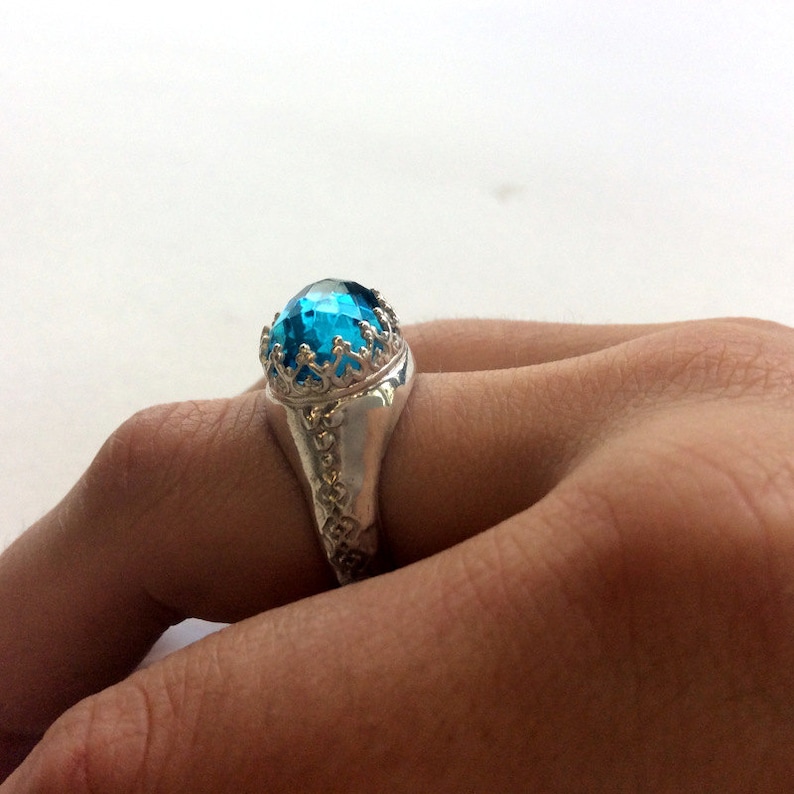 Puede incluir: Un anillo de plata con una gran piedra preciosa redonda azul engastada en un engaste decorativo de corona.
