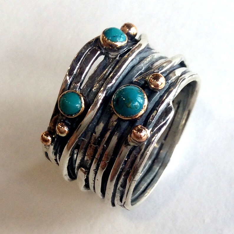 May include: A silver ring with multiple bands and turquoise stones set in the metal. The ring is accented with small gold beads.