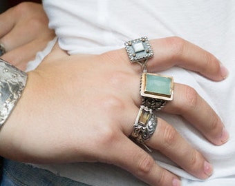 May include: Three silver rings with square settings. The top ring features a white stone, the middle ring has a light blue stone, and the bottom ring has a brown stone.