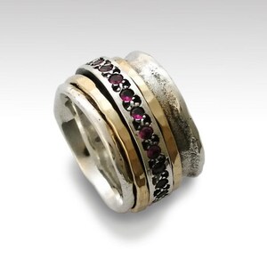 May include: A silver and gold ring with a band of pink gemstones. The ring is made of multiple bands that spin around each other.
