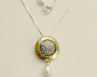 May include: A silver chain necklace with a gold and silver pendant featuring a detailed floral design. A single white pearl dangles from the bottom of the pendant.