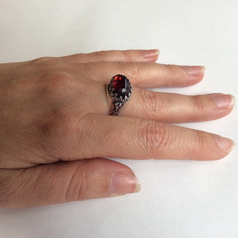 Puede incluir: Un anillo de plata con una gran piedra preciosa roja de forma ovalada engastada en un dise&ntilde;o ornamentado y detallado.