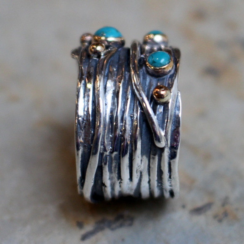 May include: A silver ring with a textured, woven design. The ring is adorned with turquoise and gold accents.