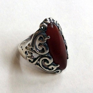 May include: A silver ring with an ornate design and a large, oval-shaped carnelian stone.