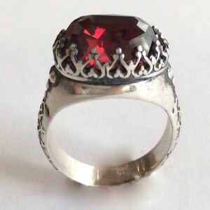 Puede incluir: Un anillo de plata con un dise&ntilde;o ornamentado y una gran piedra preciosa roja en el centro.